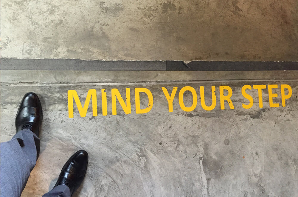 Businessman stands by "Mind Your Step" marking on office staircase